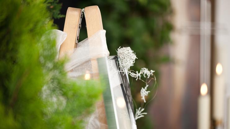 Staffelei mit einem eingewickelten Bilderrahmen und dekorativen Zweigen vor unscharfem, grünem Hintergrund.