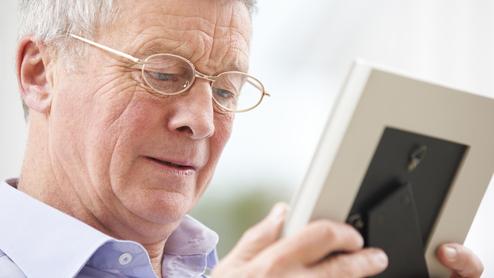 Ein älterer Mann mit Brille betrachtet ein Foto in einem Bilderrahmen.